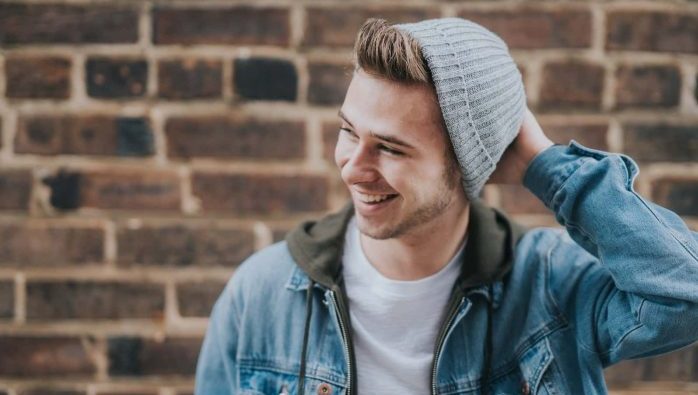 man holding the back of his head while smiling near brick wall